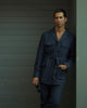 Model wearing the safari jacket in linen for men by Luxire in dark indigo leaning on wall